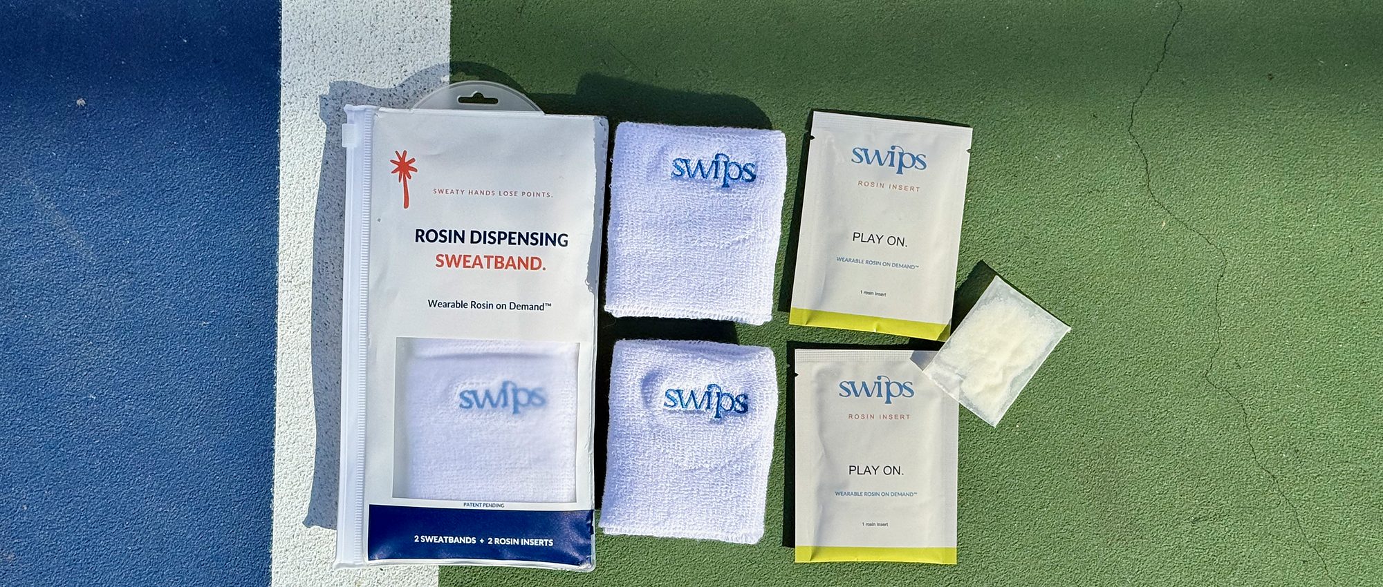 The Swips 2-pack laid out on a pickleball court: retail pouch, two sweatbands, two foil sachets and a rosin insert