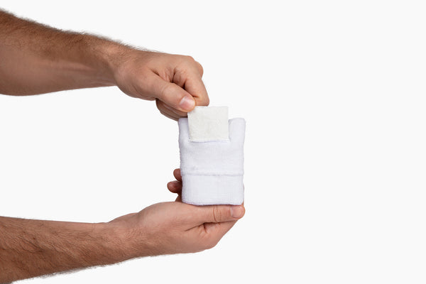 Hands sliding a Swips rosin insert into the hidden pocket of a white terry cloth sweatband