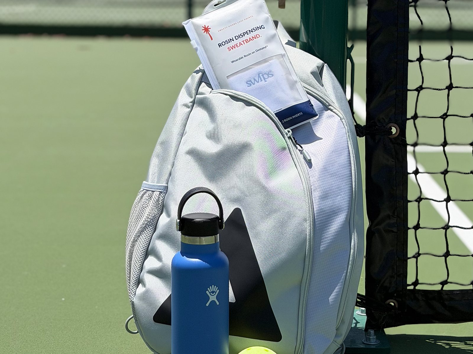 A Swips rosin insert sachet tucked into a pickleball bag beside the net, with a water bottle and a ball